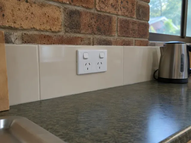 Double power point on a tiled kitchen splashback above a dark benchtop in Erina