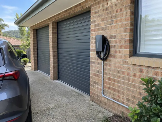 EV charger mounted on a brick garage wall beside roller doors in Wamberal