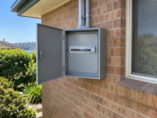 Open outdoor switchboard cabinet on a brick house wall beside a window in Green Point